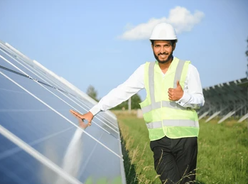 In Jaipur, Rajasthan, a man wearing a hard hat stands next to solar panels, highlighting solar energy advancements.