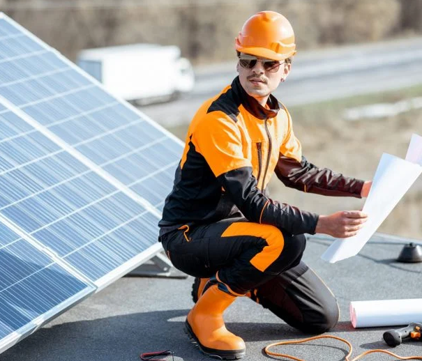  A man wearing an orange and black uniform presents a solar panel and blueprint, highlighting solar energy in Jaipur, Rajasthan.